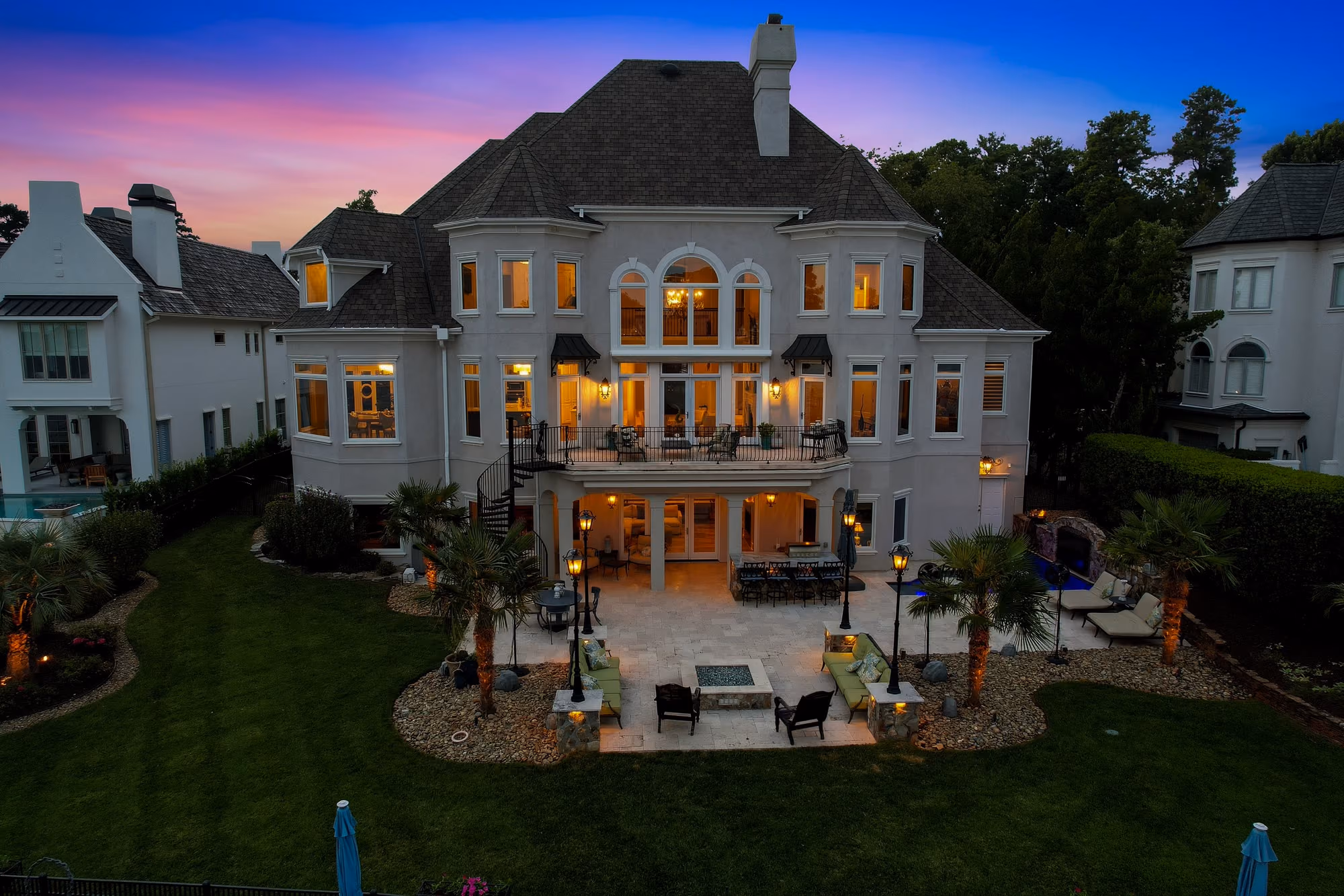 A white stucco house at dusk, its windows lit above the lawn.